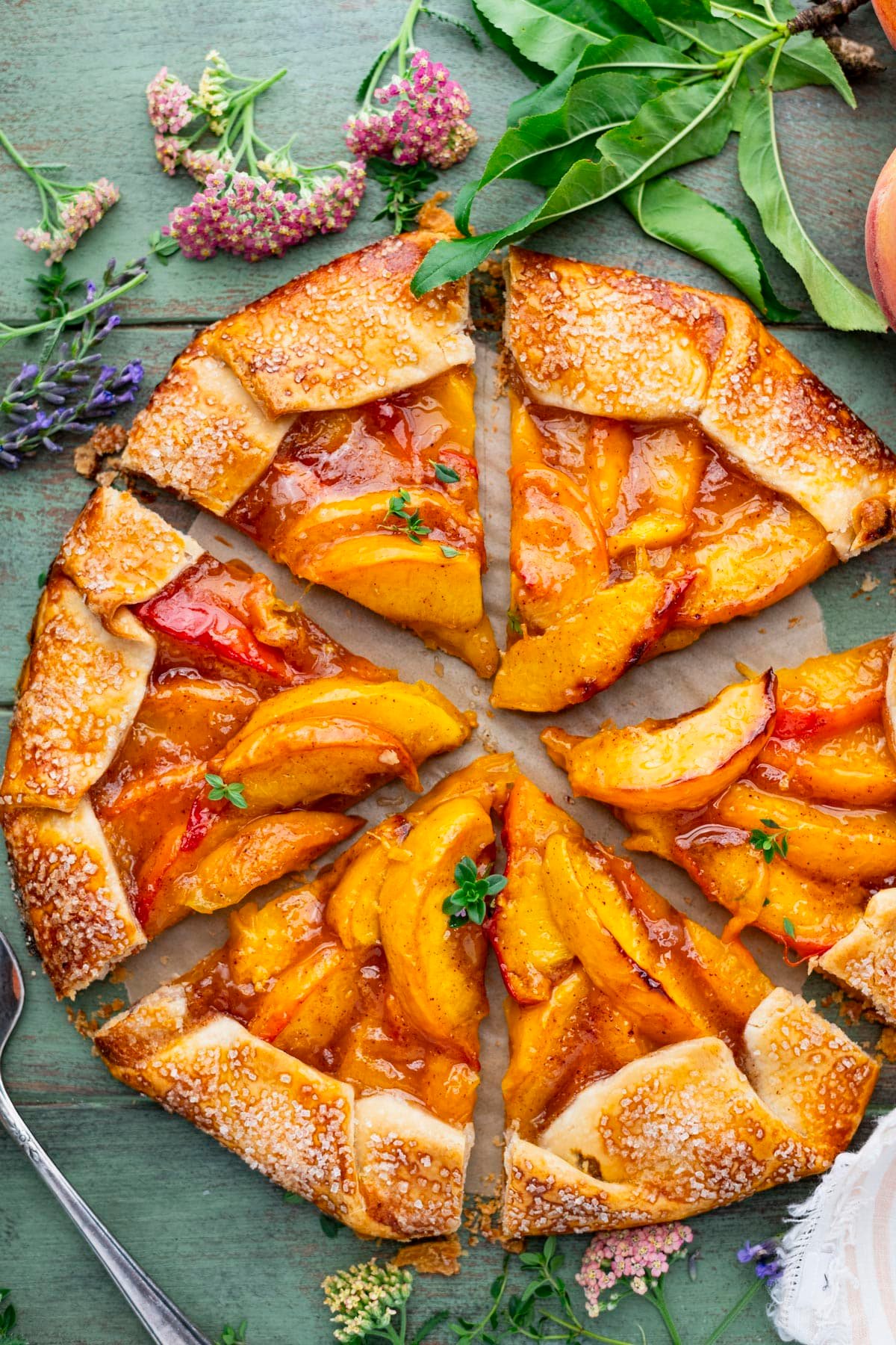 Overhead image of a sliced peach galette on a green wooden table.