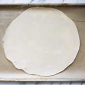 Crust for a galette on a rimmed baking sheet and parchment paper.
