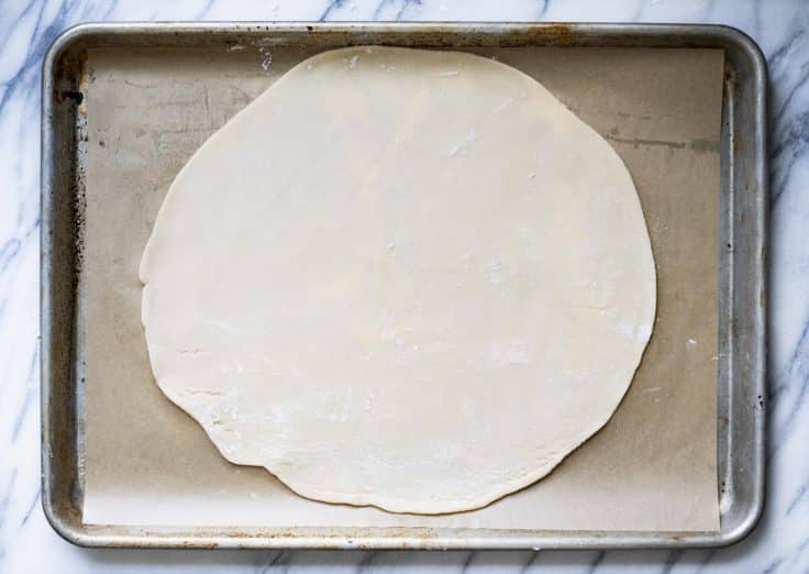 Crust for a galette on a rimmed baking sheet and parchment paper.