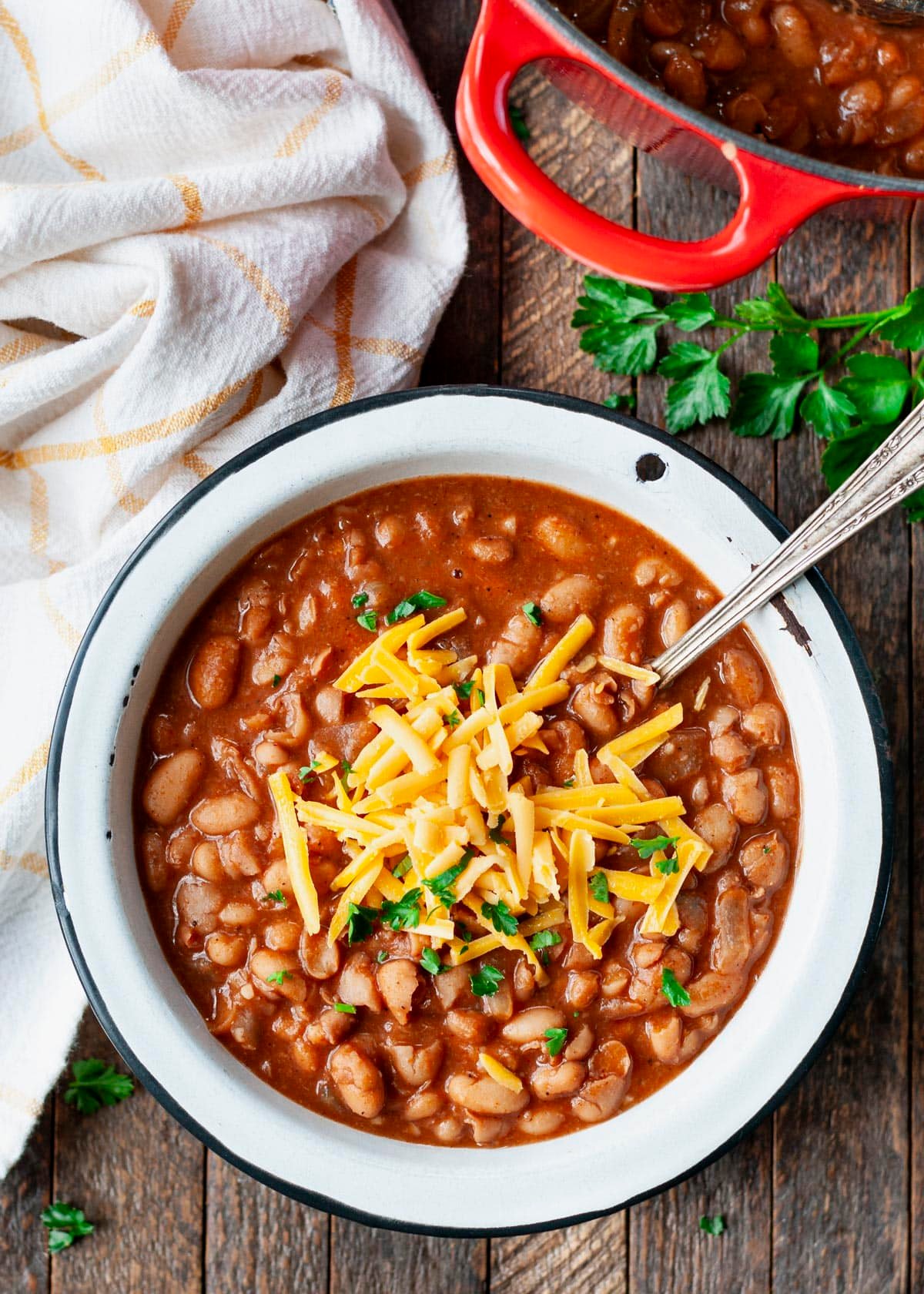 Spoon in a bowl of ranch style beans with cheese on top.