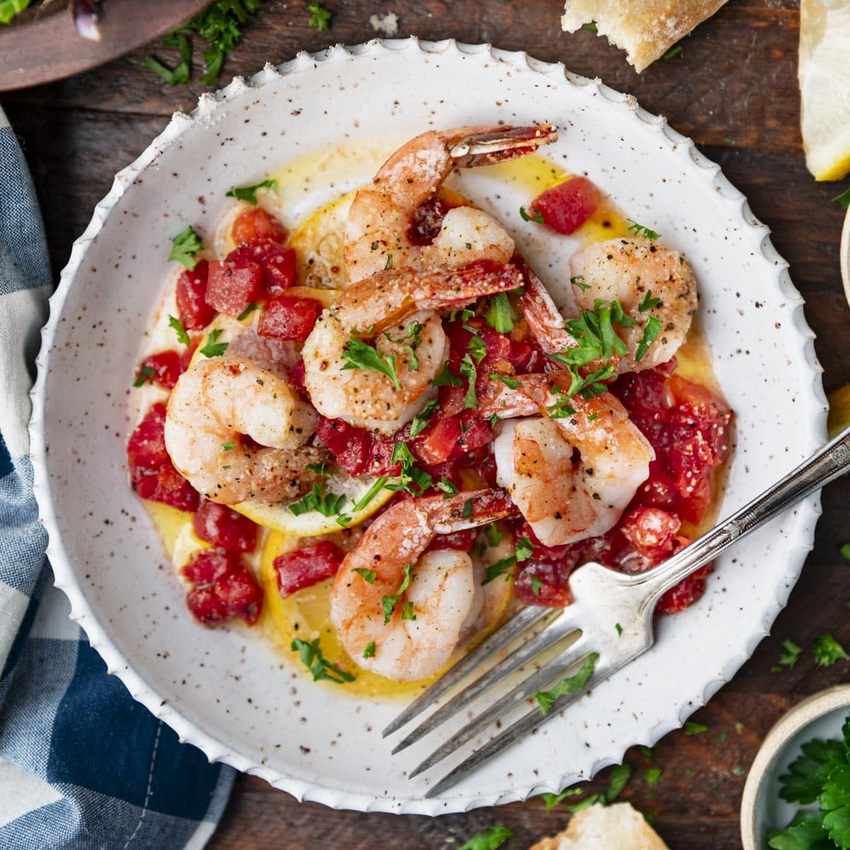 Square overhead image of a bowl of Italian shrimp with tomatoes and lemons.