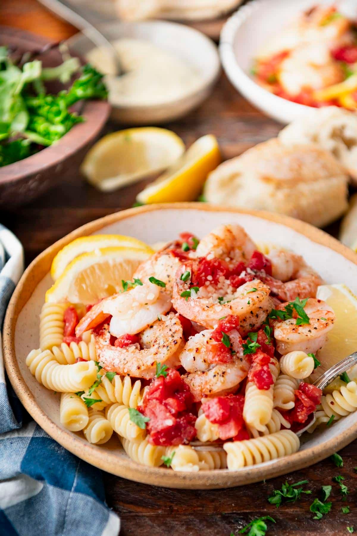 Side shot of two bowls of baked italian shrimp on a bed of pasta.