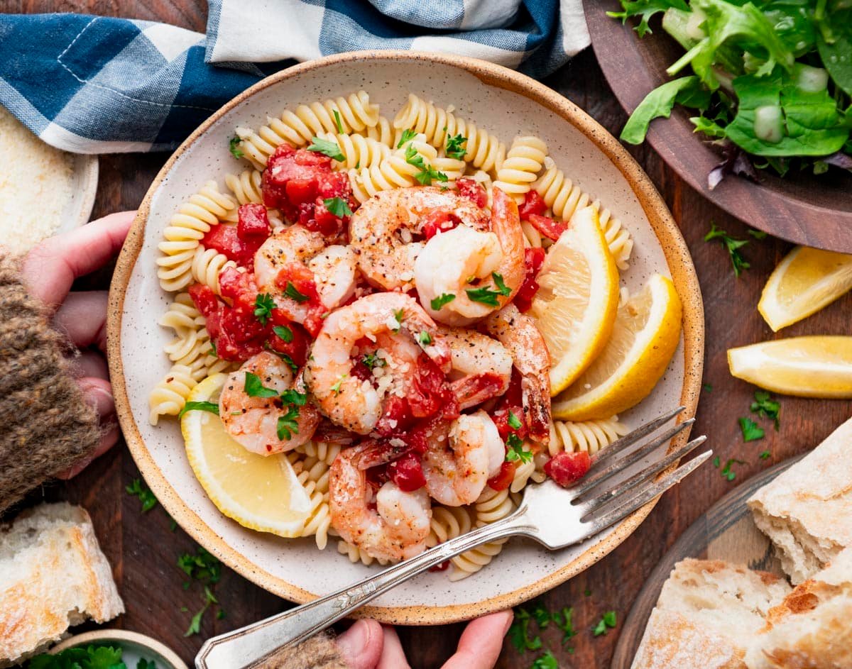Horizontal overhead image of hands holding a bowl of sheet pan Italian shrimp.