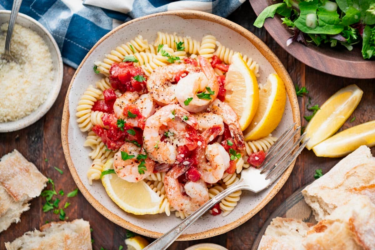 Horizontal overhead image of a bowl of baked Italian shrimp on a bed of pasta.