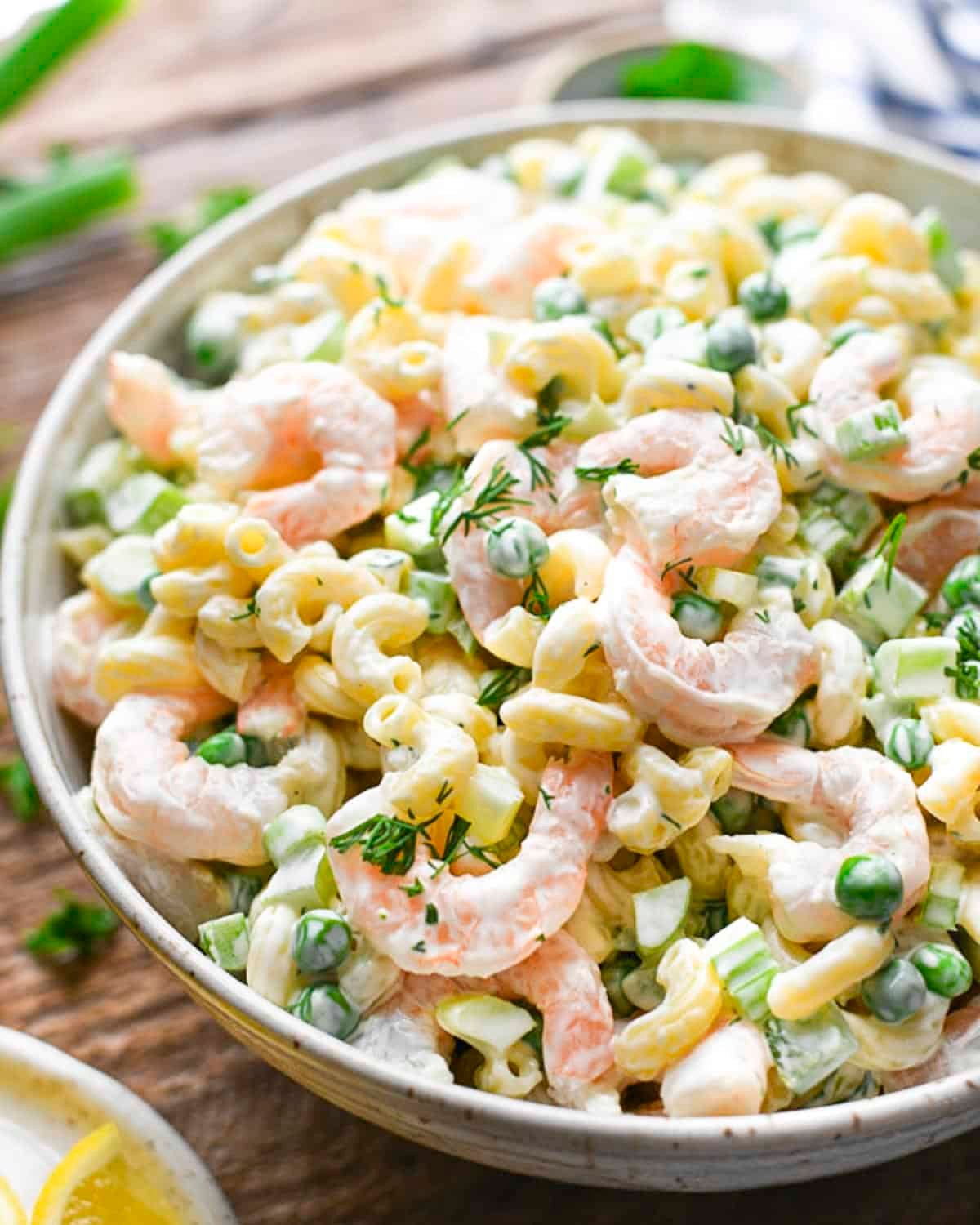 Close up side shot of a bowl of shrimp pasta salad with fresh dill for garnish.