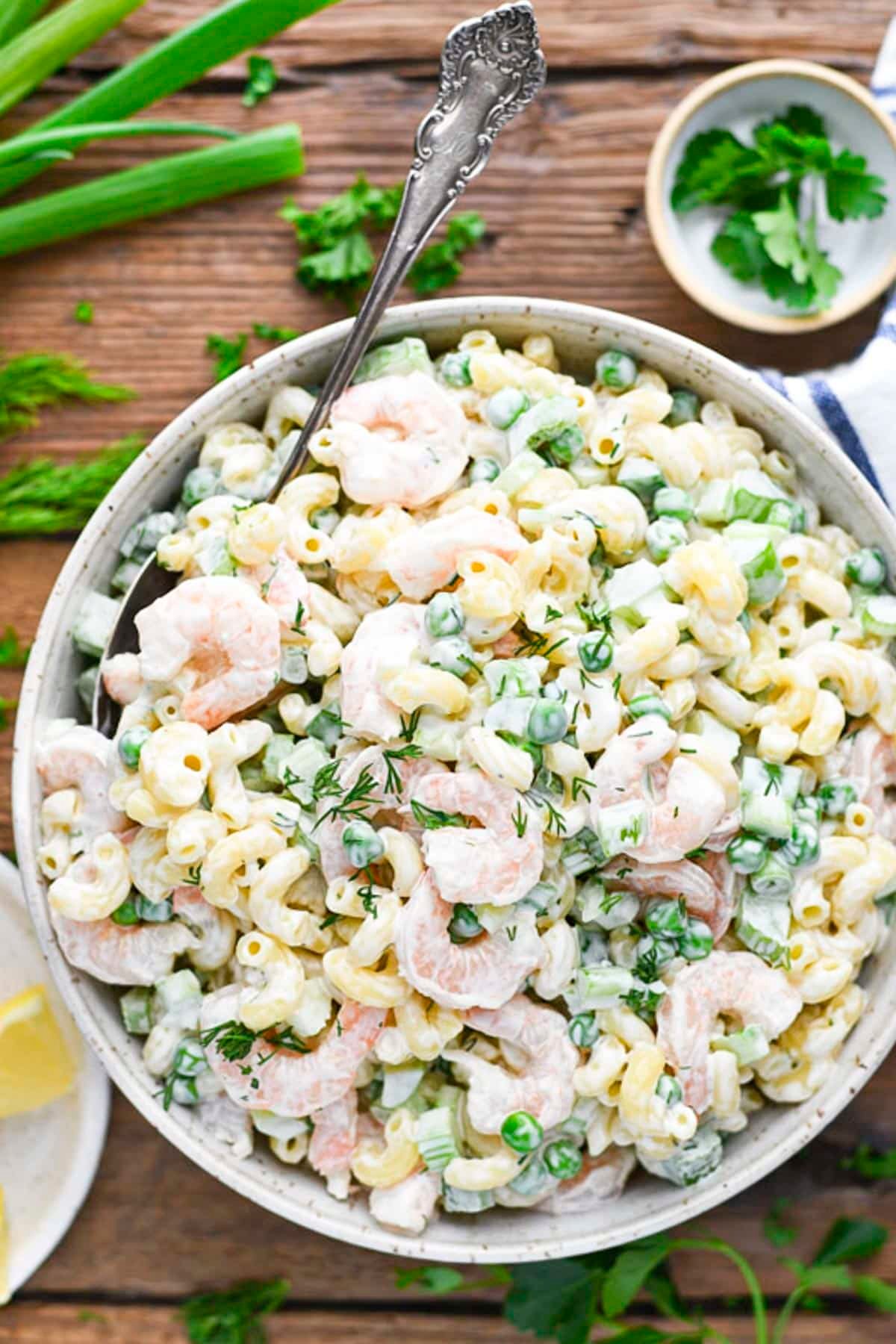 Overhead image of shrimp pasta salad recipe on a table with a side of green onions, lemon, and parsley.