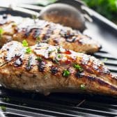Horizontal side shot of grilled chicken with a garlic and herb marinade on a grill.