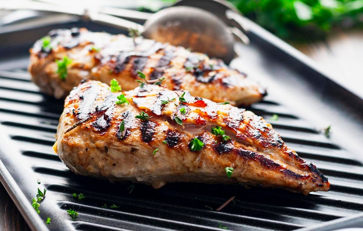 Horizontal side shot of grilled chicken with a garlic and herb marinade on a grill.