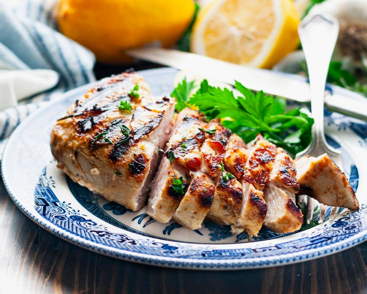 Horizontal side shot of sliced marinated grilled chicken breast on a blue and white plate.