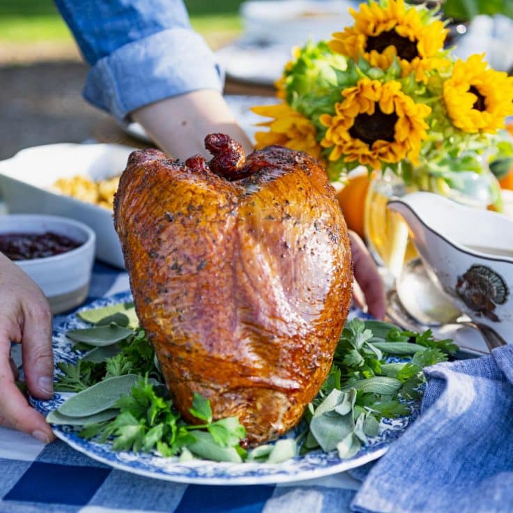 Hands serving smoked turkey breast on a holiday table.