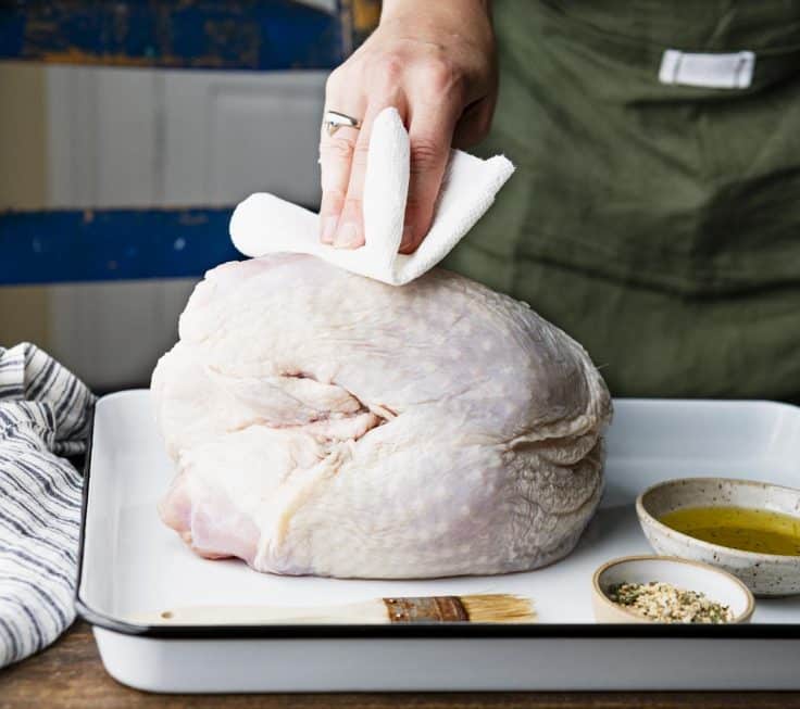 Patting a turkey breast dry with paper towels.