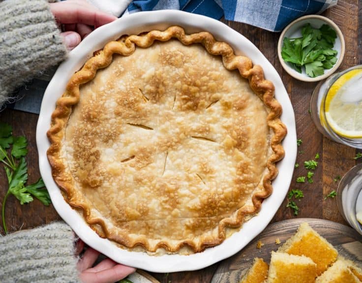 Hands holding a white pie dish full of the easiest chicken pot pie recipe ever.