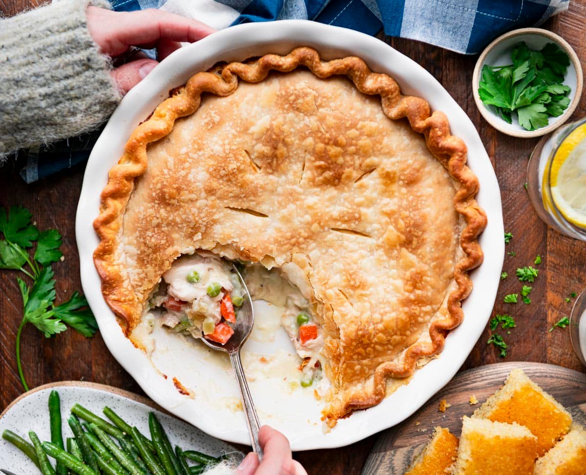 Horizontal overhead shot of hands serving Mom's easy chicken pot pie recipe on a rustic wooden table.