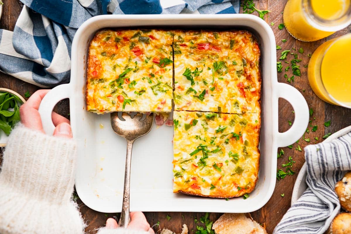 Horizontal overhead image of hands serving baked western omelette from a white dish.