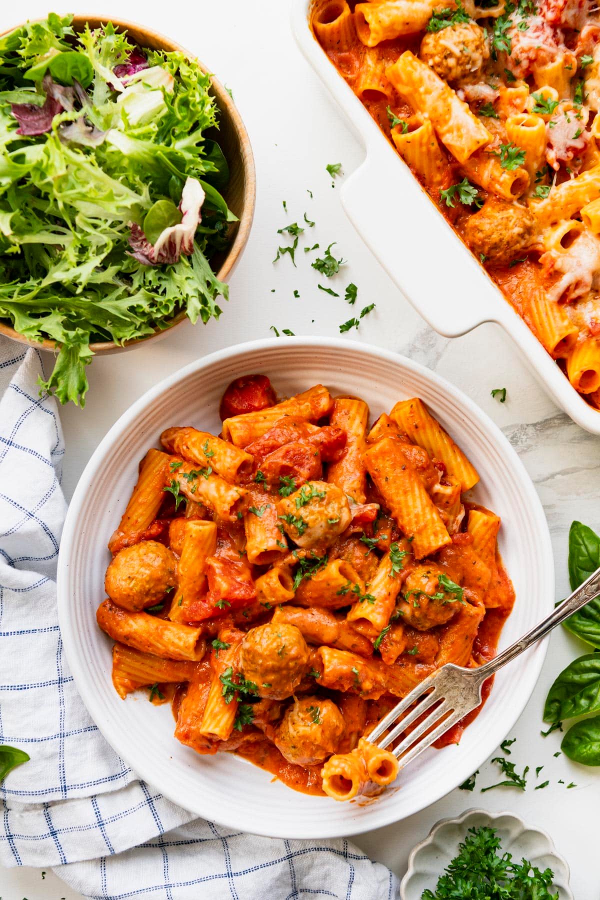 Overhead shot of a bowl of creamy tomato pasta with turkey meatballs on a white table.