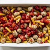 Turkey meatballs, pasta, and tomatoes in a white baking dish.