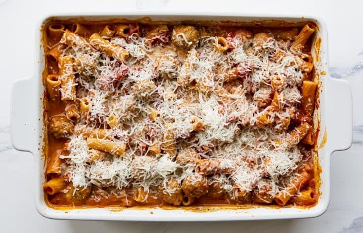 Process shot showing how to add shredded cheese to the top of a creamy tomato pasta bake.