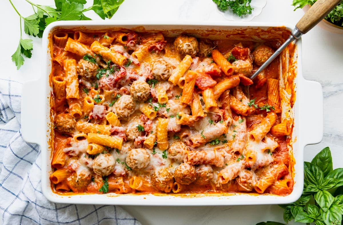 Horizontal overhead shot of a serving spoon in a white dish full of creamy tomato pasta with turkey meatballs.