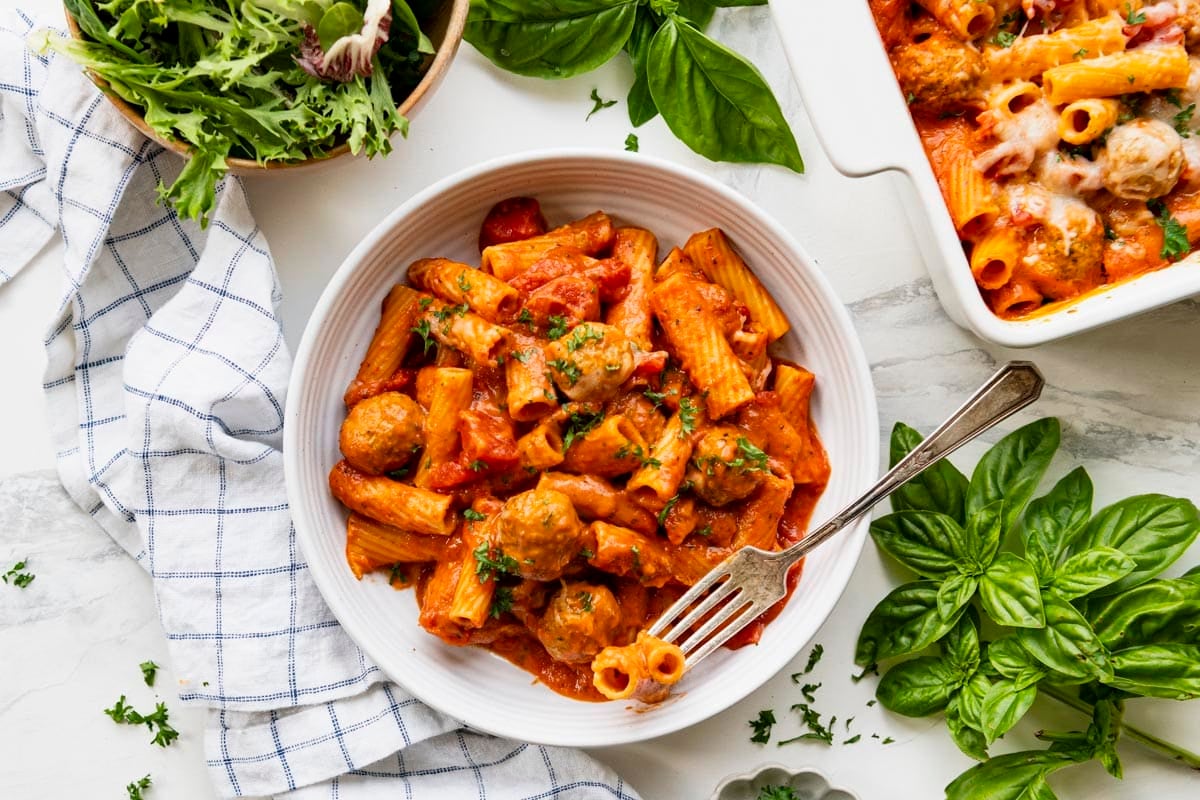 Horizontal overhead shot of creamy tomato pasta with turkey meatballs in a white bowl on a white table.