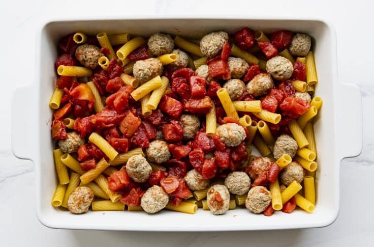 Turkey meatballs, pasta, and tomatoes in a white baking dish.