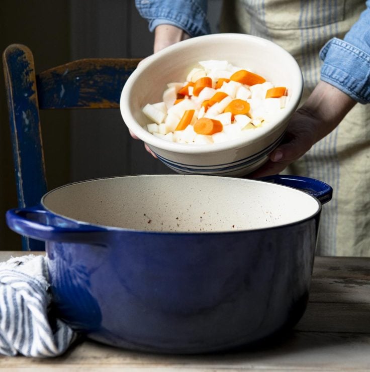 Adding vegetables to a dutch oven.