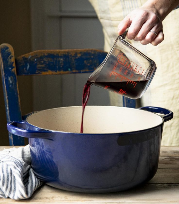 Pouring red wine into a cast iron dutch oven.