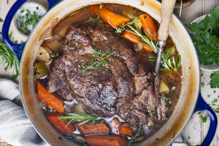 Close overhead image of a serving spoon in a dutch oven with pot roast and vegetables.