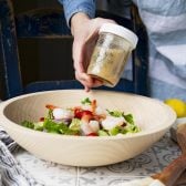 Shaking homemade Greek salad dressing in a glass mason jar.