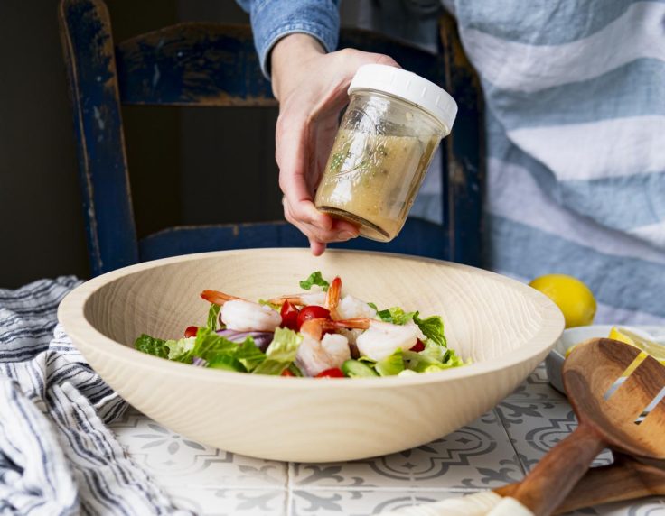 Shaking homemade Greek salad dressing in a glass mason jar.