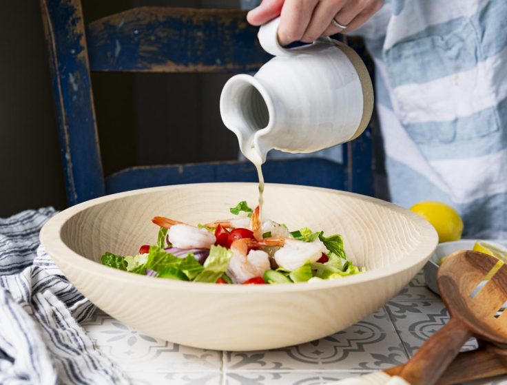 Pouring homemade greek salad dressing on a salad.