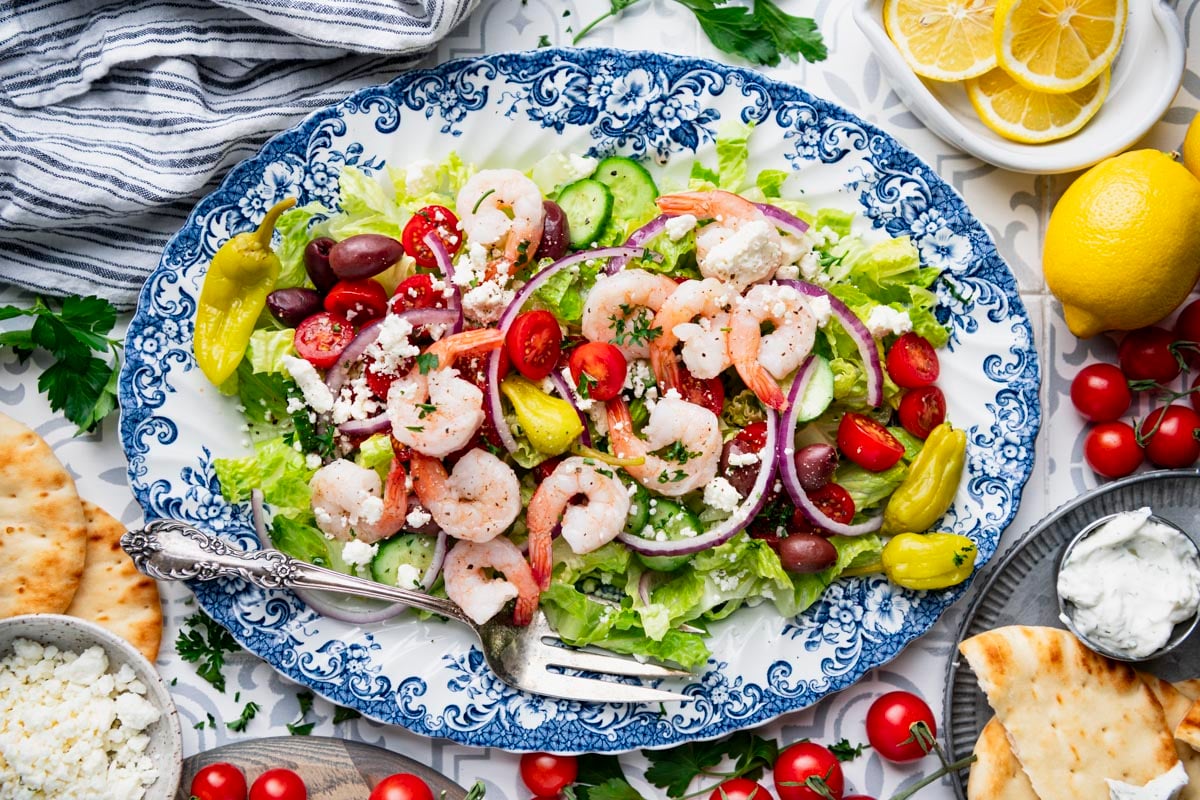 Horizontal overhead image of a blue and white platter of greek shrimp salad with a side of pita bread.
