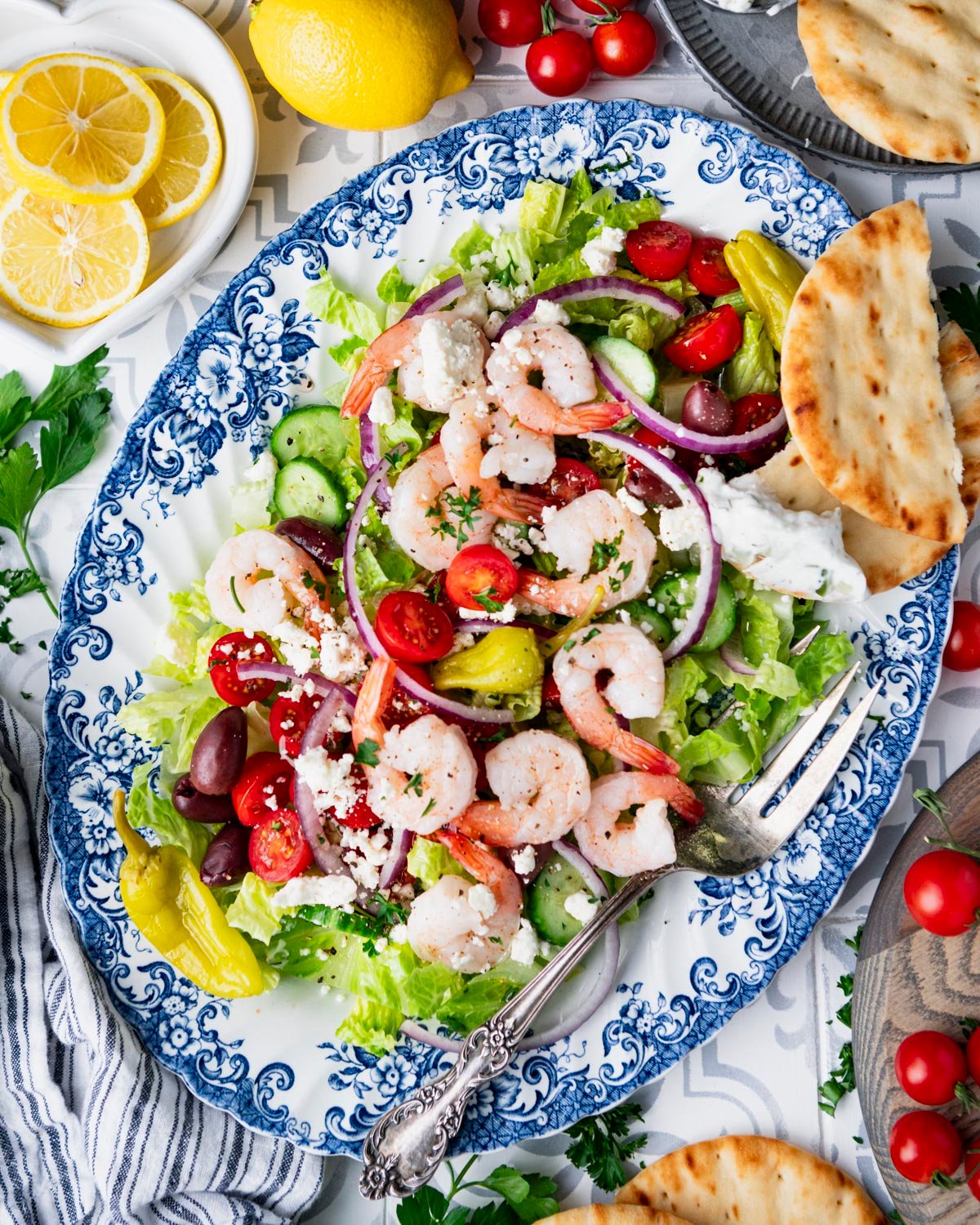 Overhead image of greek salad with shrimp and a side of pita bread and hummus.