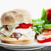 Horizontal side shot of a white plate with a chicken caprese sandwich.