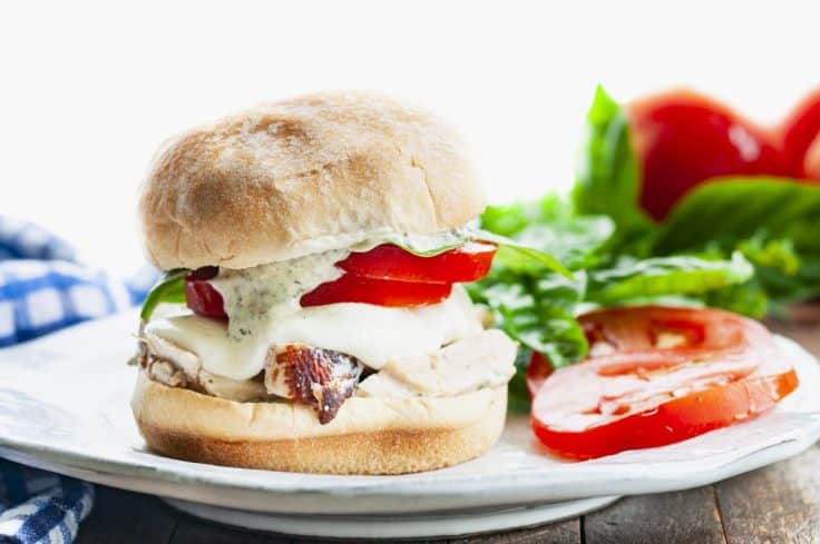 Horizontal side shot of a white plate with a chicken caprese sandwich.