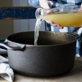 Pouring chicken broth into a cast iron dutch oven.