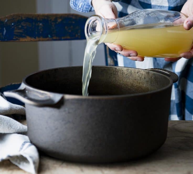 Pouring chicken broth into a cast iron dutch oven.