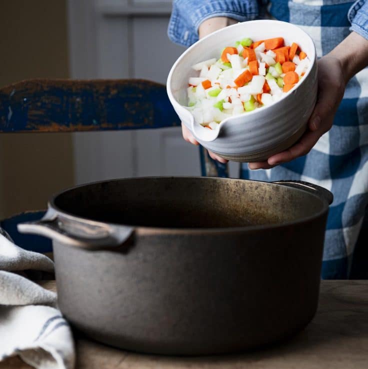 Adding vegetables to a cast iron Dutch oven.