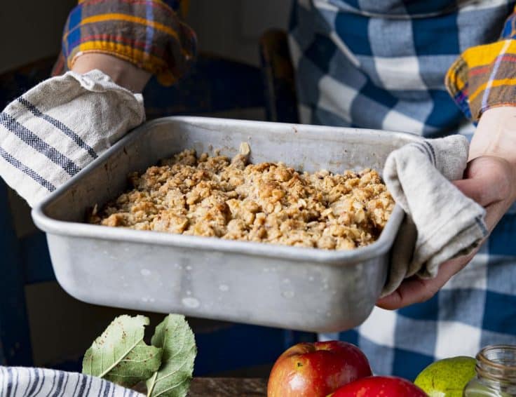 Hands holding a baked pan of pear crisp.