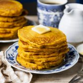Square side shot of a stack of pumpkin pancakes with butter and syrup on a blue and white plate.