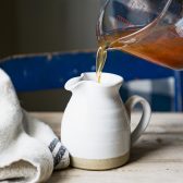 Pouring apple cider syrup into a white pitcher.
