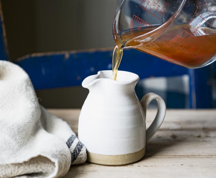 Pouring apple cider syrup into a white pitcher.