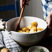 Stirring gold potatoes in a white bowl with olive oil, garlic, and rosemary.