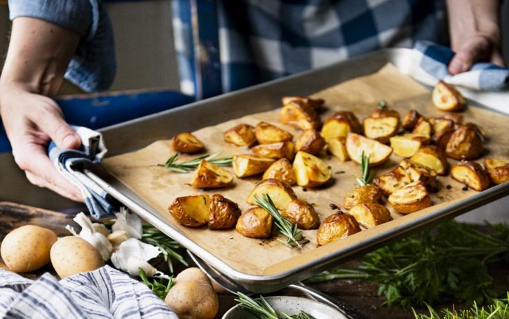 Hands holding a baking sheet full of rosemary roasted potatoes.