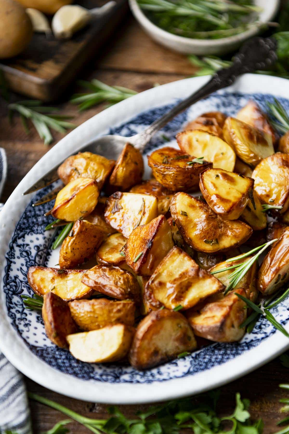 Close up side shot of a blue and white tray full of roasted potatoes with rosemary and olive oil.