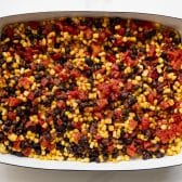 Corn, black beans, diced tomatoes, and seasoning in a white baking dish.