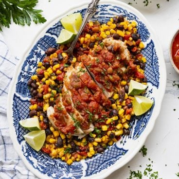 Square overhead shot of salsa chicken on a blue and white platter with corn, tomatoes, and black beans.
