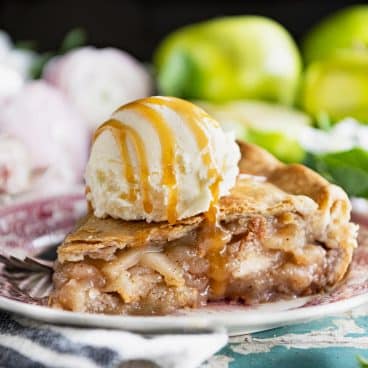 Square side shot of a slice of easy apple pie with a scoop of vanilla ice cream and a drizzle of caramel sauce on top.