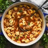 Ladle in a Dutch oven full of meatball tortellini soup.