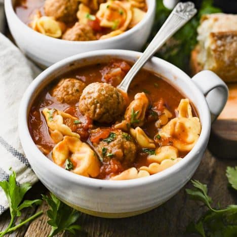 Square shot of a spoon in a bowl of meatball tortellini soup.